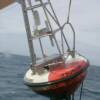 The surface mooring uses a 2.5 m diameter fiberglass over foam disk buoy with a gross displacement of 4000 kg. The mooring line is 19 mm 8-strand plaited nylon line with a rated breaking strength of 7100 kg and is deployed with a scope of 0.985.
